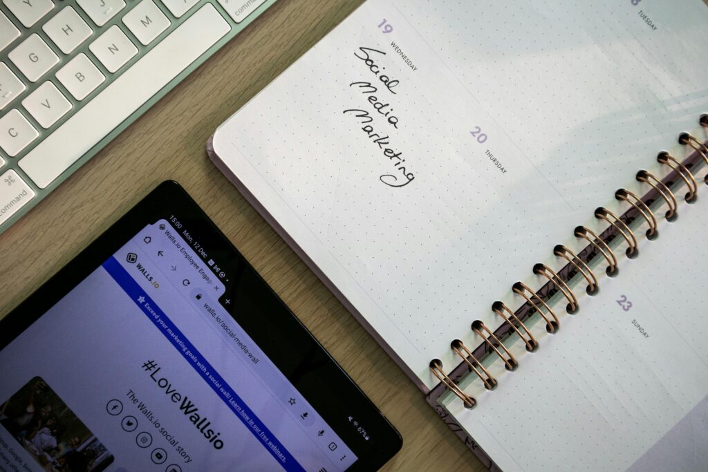 Flat lay of a workspace with a keyboard, a tablet displaying a social media page, and an open planner showing a handwritten note that reads 'Social Media Marketing' scheduled on Wednesday the 19th. Best Social Media Marketing Agency