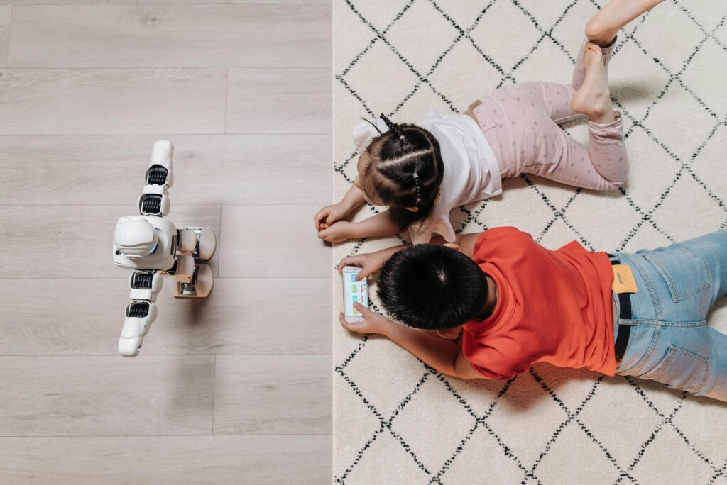 Two children lying on the floor interacting with a robot and a tablet, showcasing how the Best AI Tools make learning and play more engaging through technology.