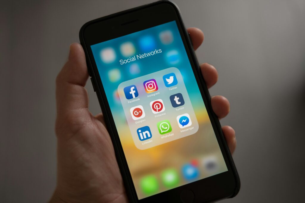 metapay ads A person holding a smartphone displaying a folder labeled "Social Networks" with app icons for Facebook, Instagram, Twitter, Google+, Pinterest, Tumblr, LinkedIn, WhatsApp, and Messenger.